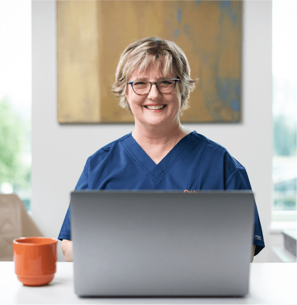 Smiling nurse in blue scrubs working on a laptop