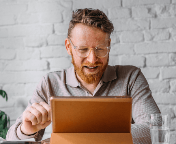 Man with red hair and glasses using a tablet, checking his Optum healthcare information.