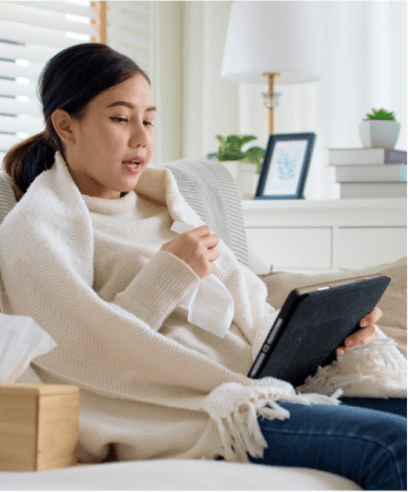 Sick woman wrapped in a blanket using a tablet at home