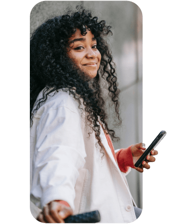 Smiling woman in a white coat holding a smartphone and an electric scooter