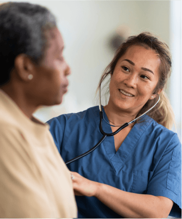 Smiling nurse in blue scrubs using a stethoscope on a patient