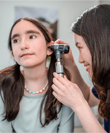 Female doctor at Optum OR examining a young girl's ear with an otoscope during a medical check-up.